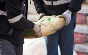 Two construction workers carry a bag of cement midsection close up at the warehouse
